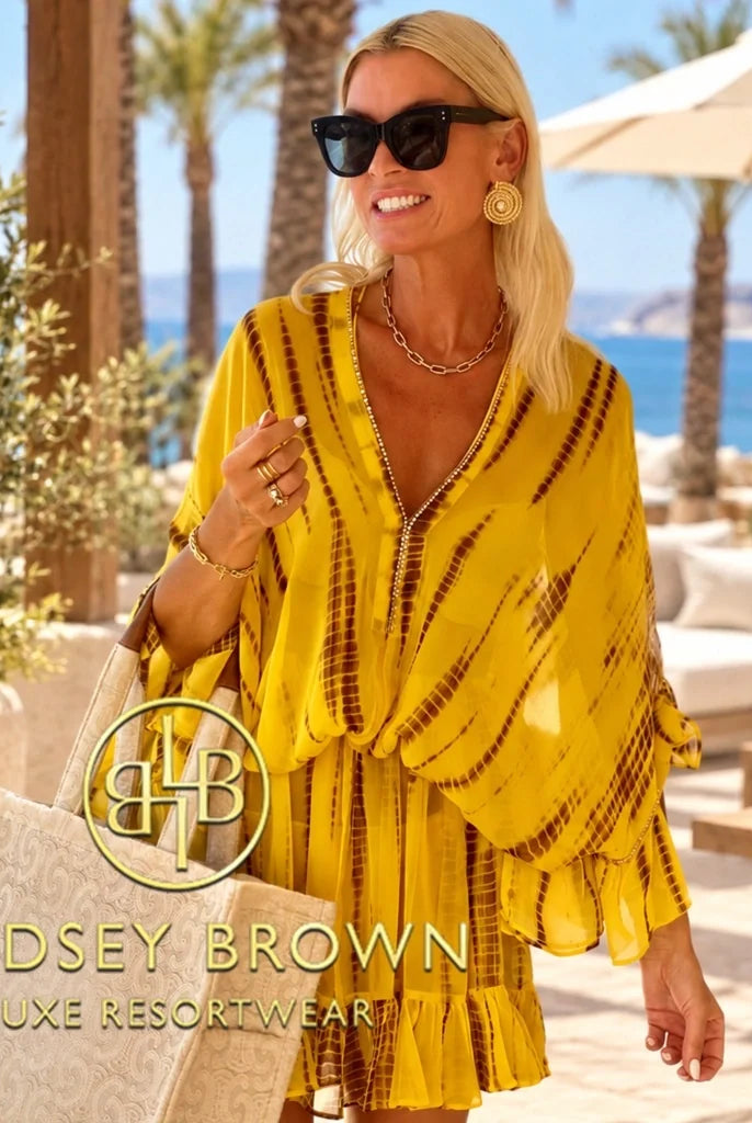 Lindsey Brown luxury resort wear branded designer silk and cotton kaftans collection image featuring a model wearing a vibrant yellow tie-dye silk kaftan dress with gold embellishments at a luxury beach resort.