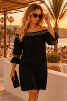 Lindsey Brown luxury resort wear featuring a model wearing an embellished black crinkle cotton off-the-shoulder beach dress at a luxury resort terrace at sunset.