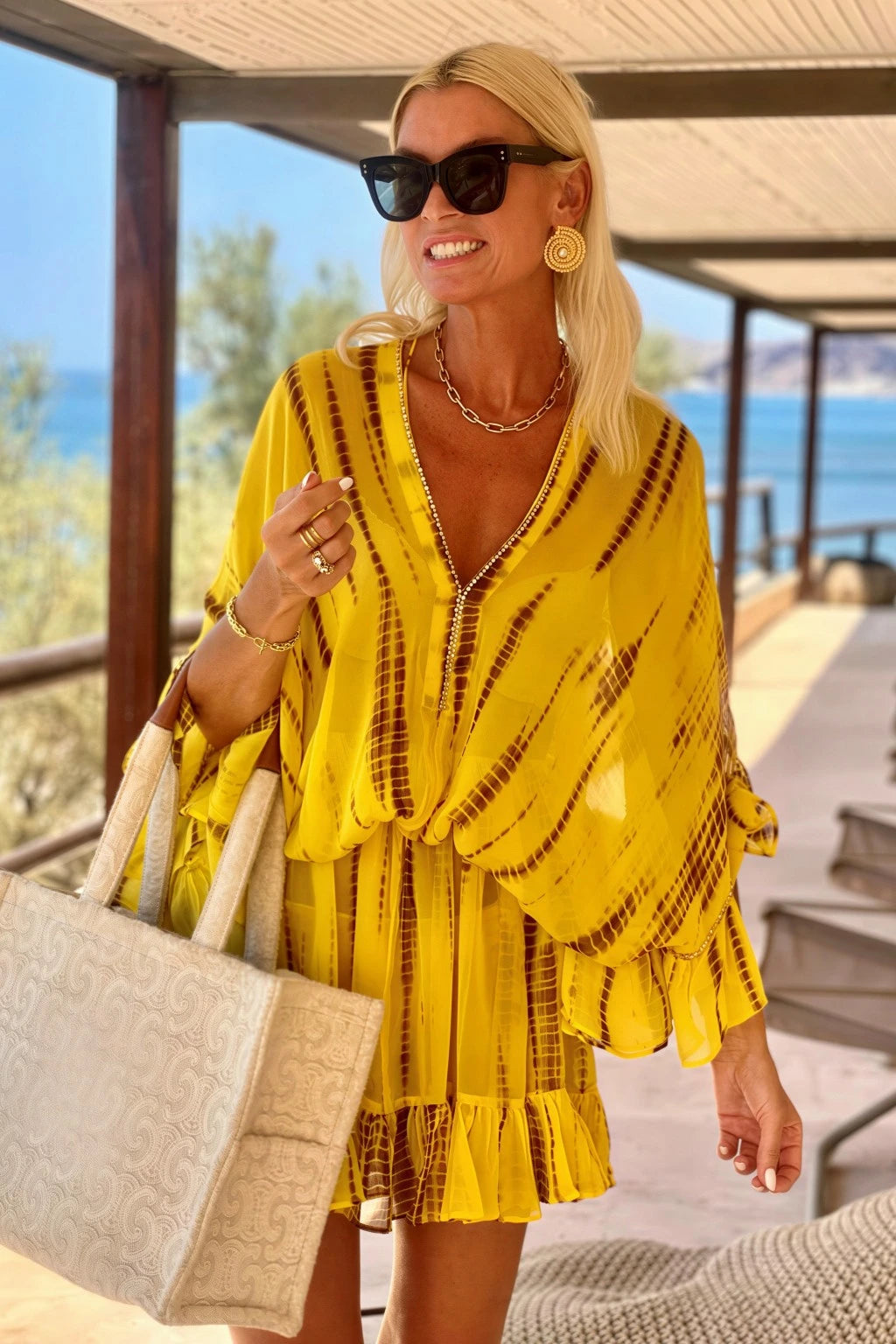 Lindsey Brown luxury resortwear featuring a model wearing a vibrant yellow tie-dye silk kaftan dress with gold embellishments at a luxury beach resort.